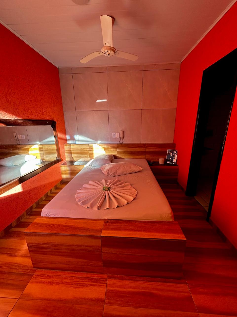 Suíte vermelha com cama de casal e piso em madeira