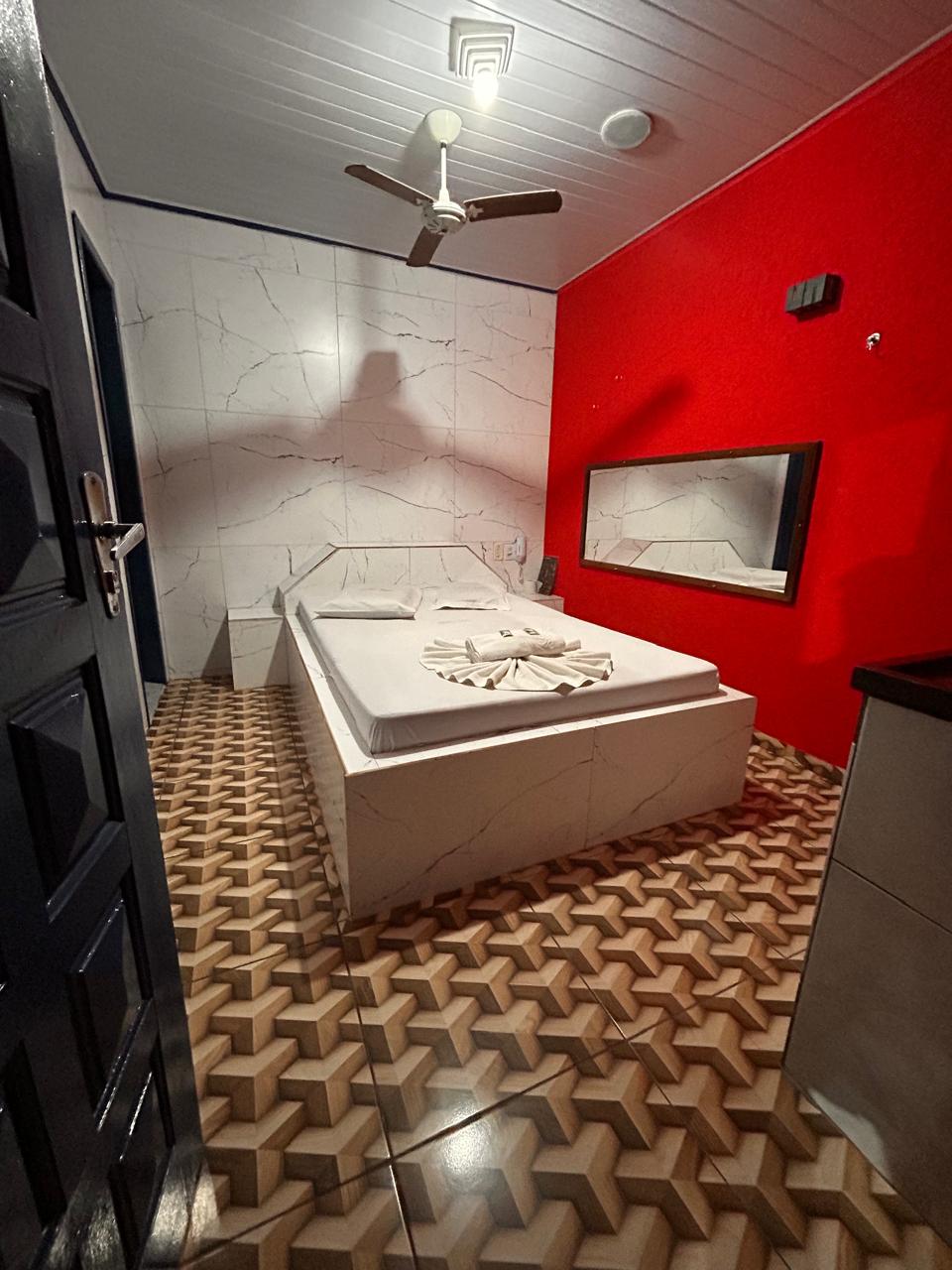 Suíte com parede vermelha, cama de casal e acabamento em mármore